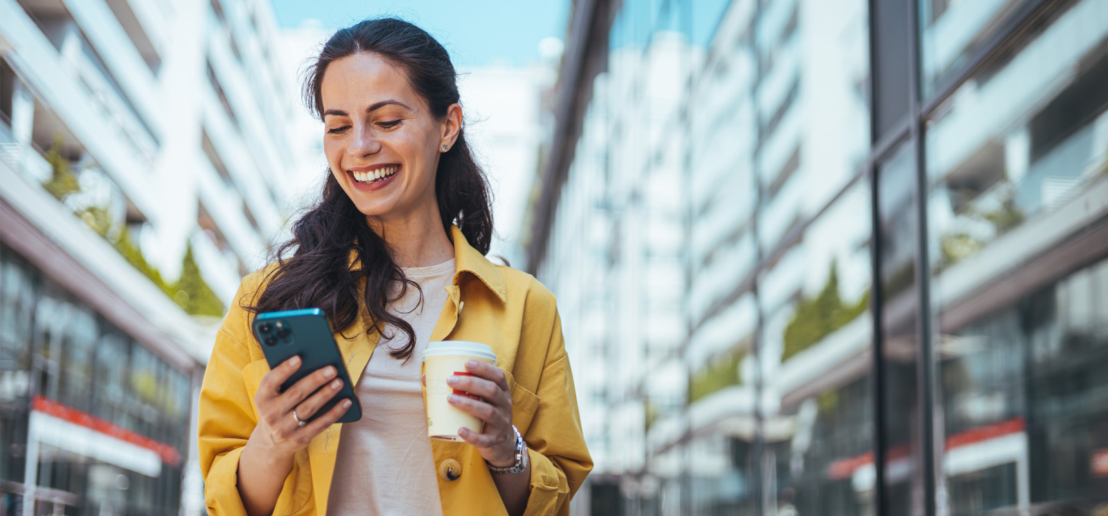 Smiling woman holding a coffee while looking at her cell phone