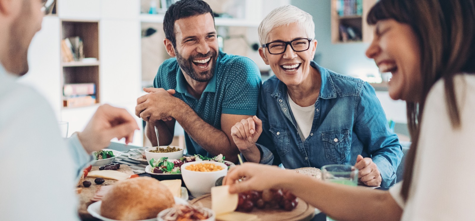 A group of people laughing with lots of food on the table in front of them.