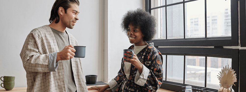 Two people holding coffee cups and standing in front of a window.