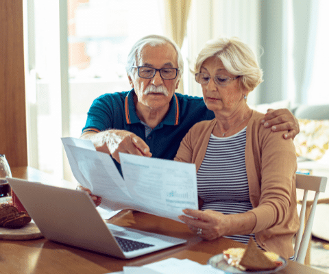 Senior couple sitting in front of lap top reviewing financial paperwork