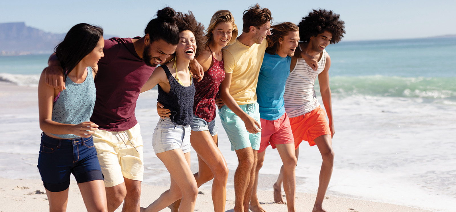 Group of seven friends on the beach walking along the ocean surf.