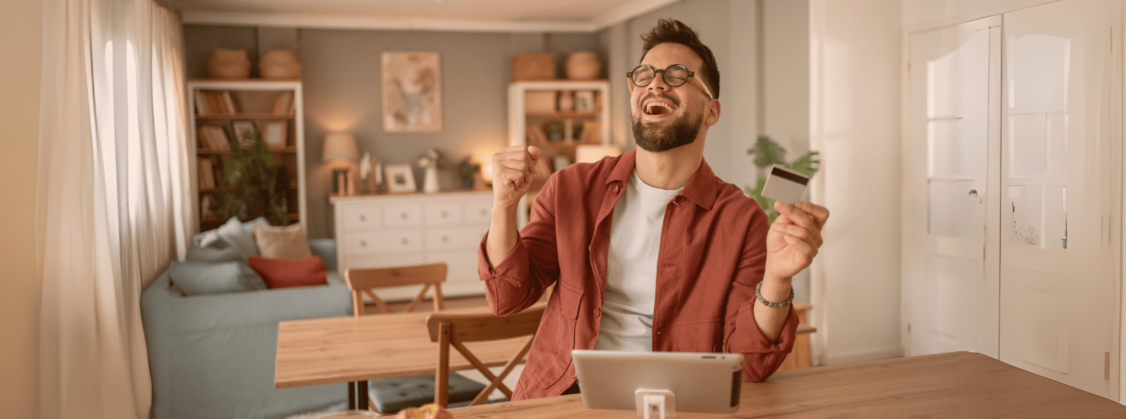 Smiling man holding a Debit Card and using a computer tablet.