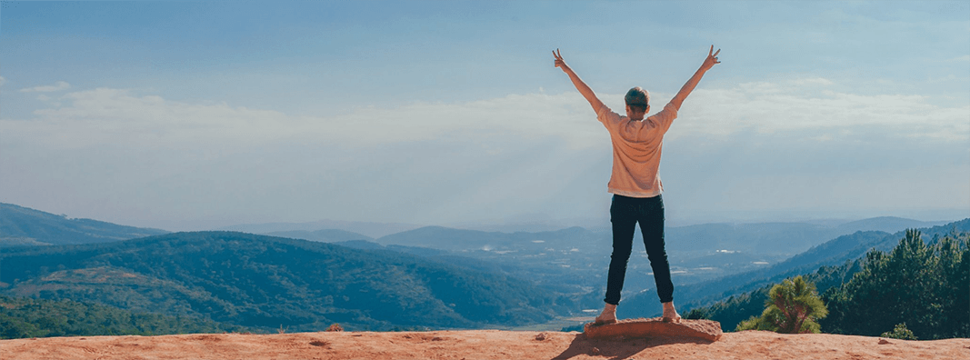 Woman with arms extended standing on a mountain top overlooking a valley