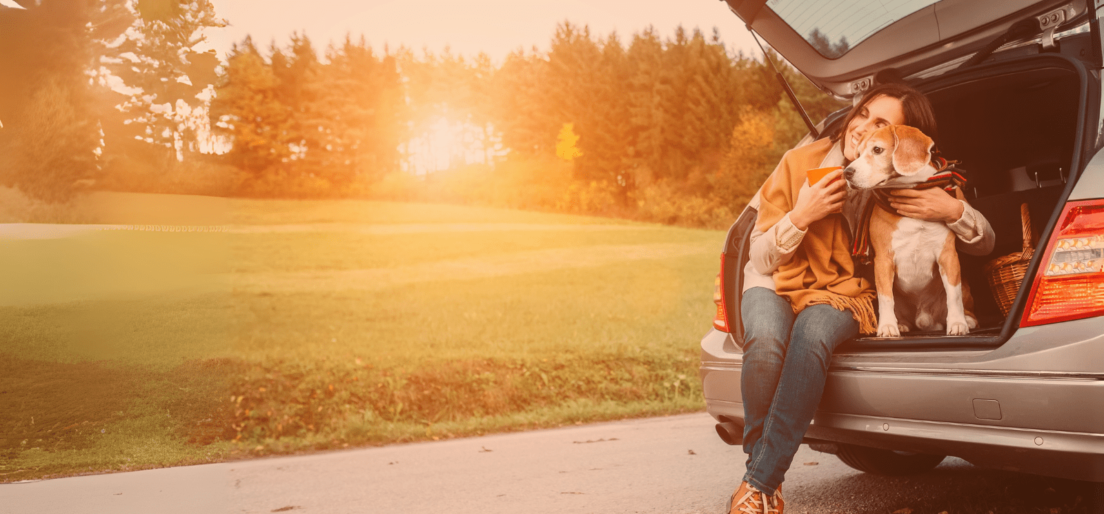 Smiling adult female sitting with a dog on the back of an SUV.