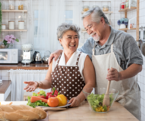 Smiling husband and wife in the kitchen making a salad.