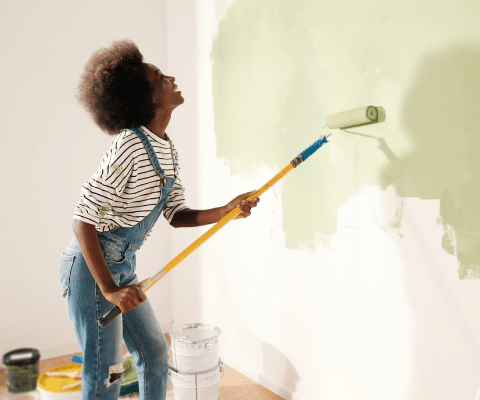 Woman wearing overalls and painting wall green
