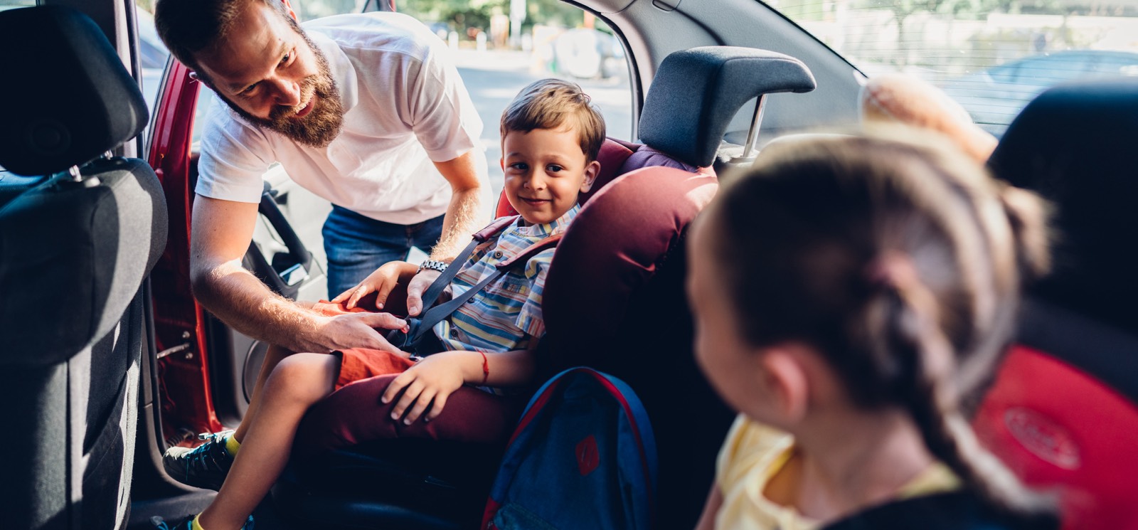 A dad buckling his young children into the back of a car.
