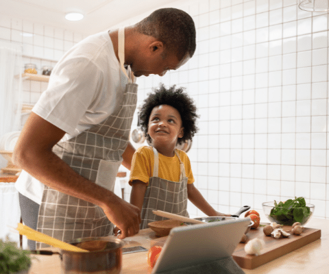 Dad and child wearing matching aprons in the kitchen making a salad