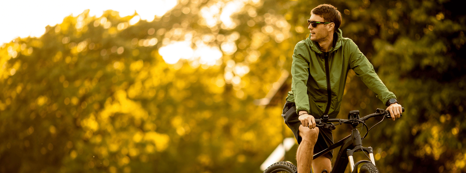 Man riding a bicycle with trees behind him.