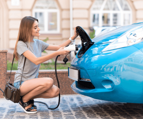 Woman in front of a blue car with charging cable plugging into car