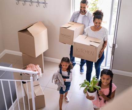A family of four carrying boxes while moving into a new home.