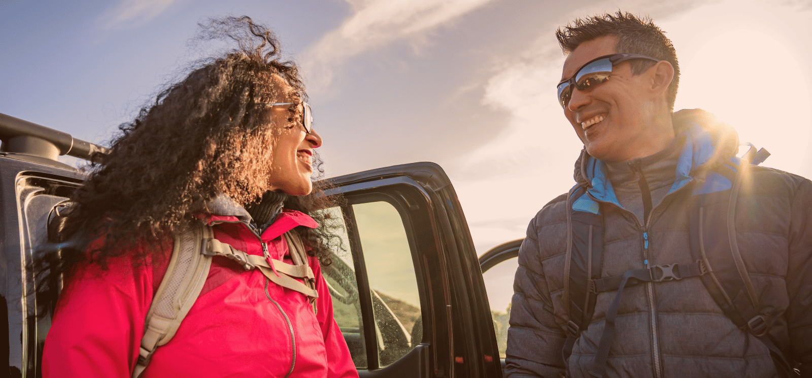 Smiling couple wearing sunglasses and standing by car.