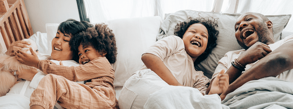 Family of four laughing while laying in bed.