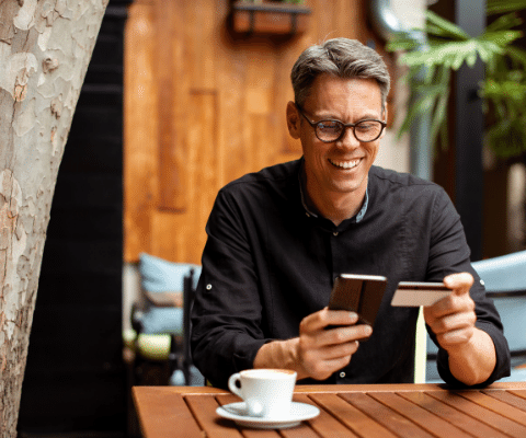 Man smiling and sitting at table with a cell phone and holding a credit card