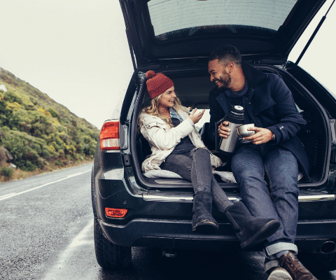 Couple smiling and sitting in the back of an SUV auto.