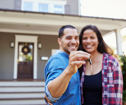 Couple holding a pair of keys outside of a new house.
