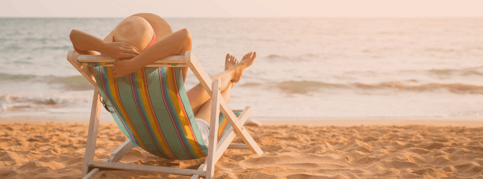 Person sitting in a sand chair on the sand facing the ocean.