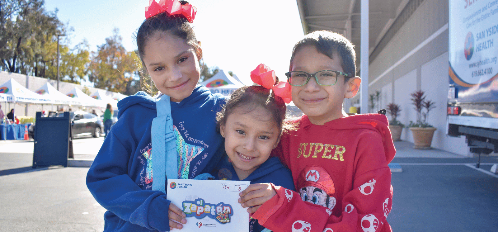 Three kids smiling and holding a donation sign for El Zapaton.