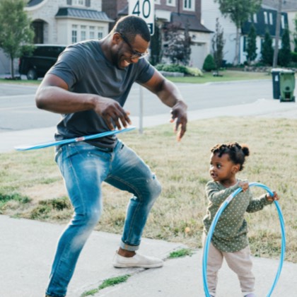 A dad playing hula hoop with his young daughter.