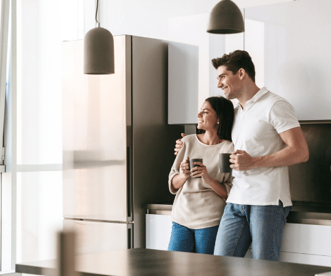 Couple in kitchen holding coffee cups and looking towards windows