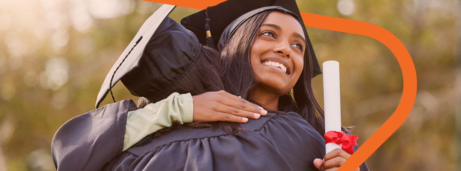 Graduating female college student wearing a cap and gown, holding a rolled-up paper, and hugging a person.