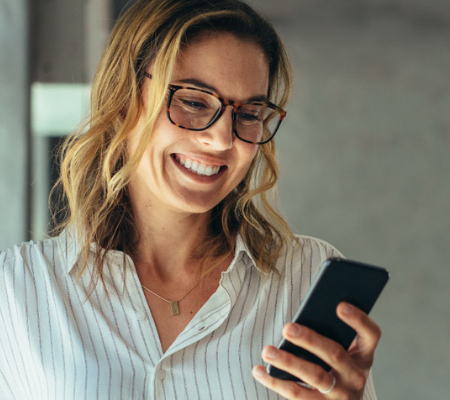 Woman smiling while looking at her cell phone in her hand.