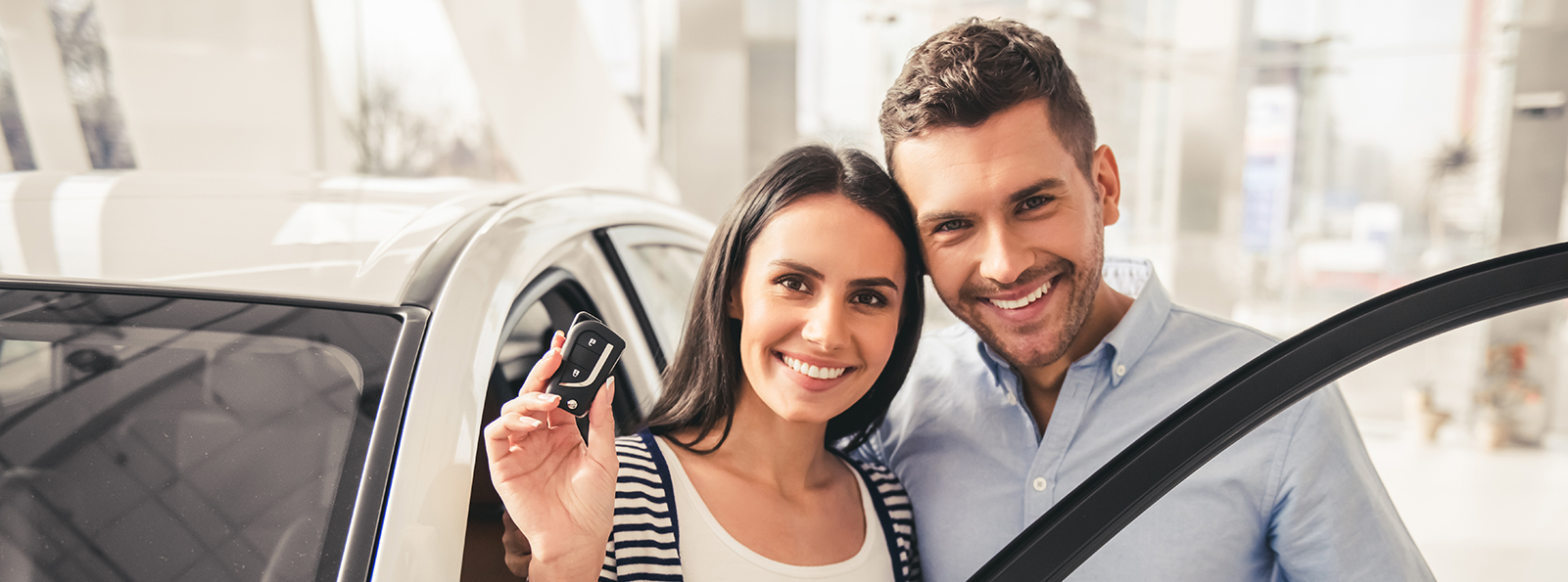 Smiling couple standing next to a car holding the keys to the car.