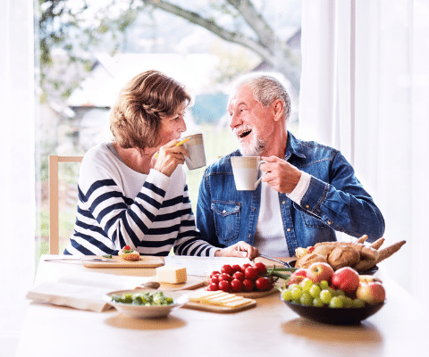 Senior couple sitting at the table with fruit and holding coffee mugs