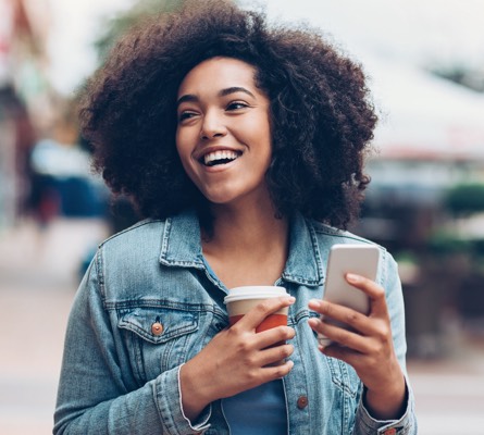 A woman holding a coffee cup and a smartphone.