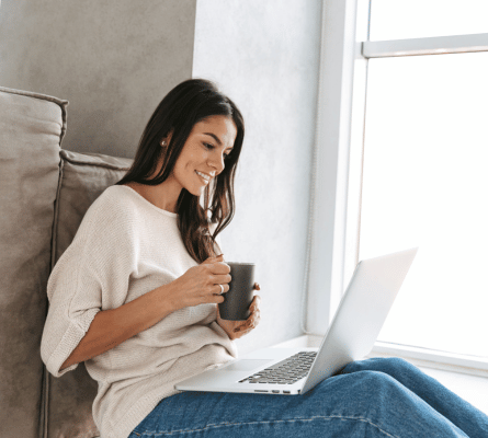 Woman sitting on the ground with a lap top and holding a cup of coffee.