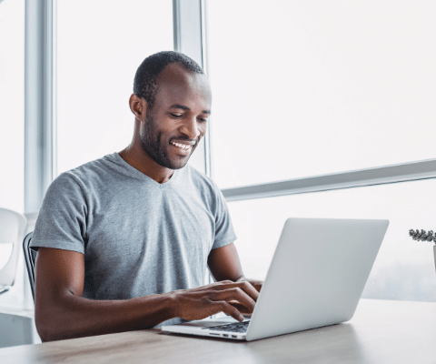 Man smiling while using laptop sitting at a table.
