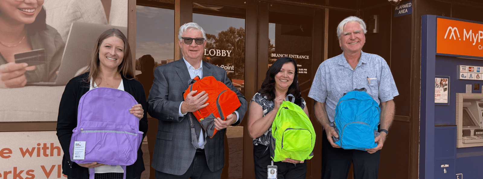 Four team members holding backpacks in front of a MyPoint branch.
