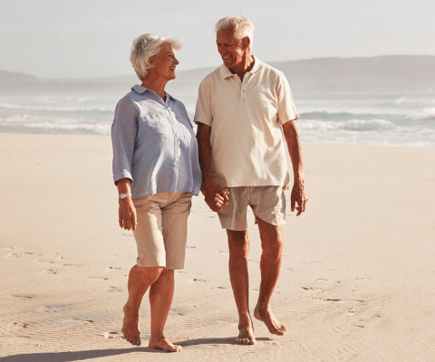 Senior couple holding hands and walking in the sand on the beach